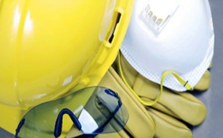 Safety equipment including a yellow hard hat, protective goggles, mask, and gloves on a table.