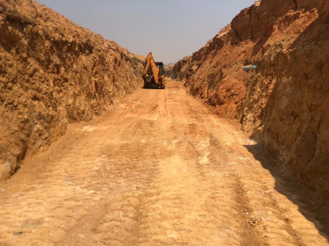 Excavator in a wide dirt trench with high walls on both sides under a clear sky.